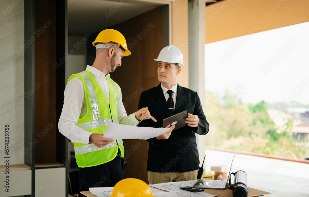 Contractor and architect looking at plan, tablet, laptop and talking about working on big project. B