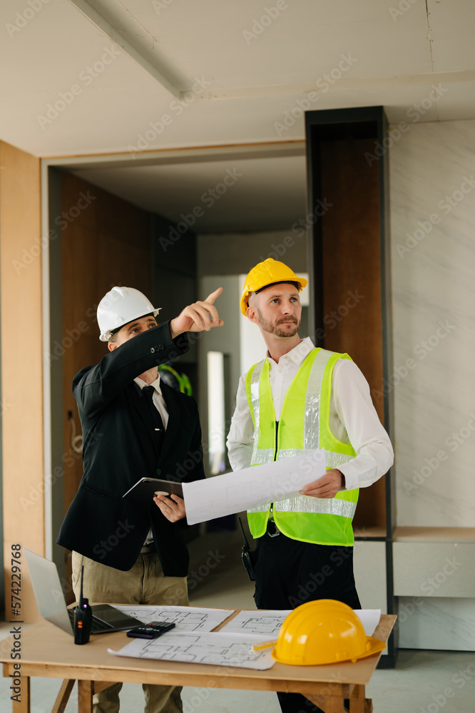 Contractor and architect looking at plan, tablet, laptop and talking about working on big project. B