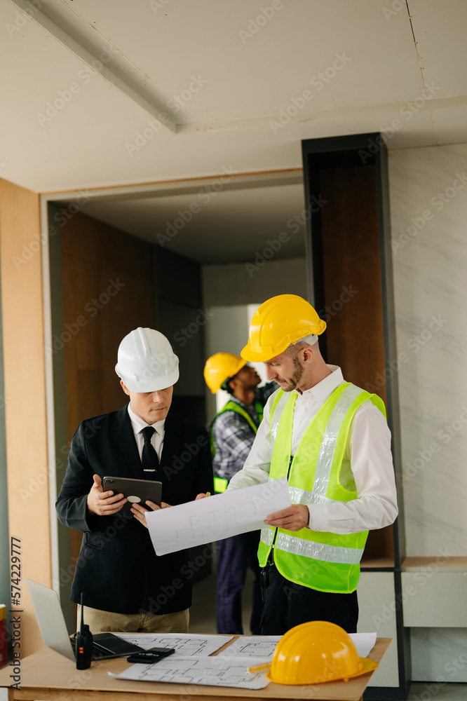 Contractor and architect looking at plan, tablet, laptop and talking about working on big project. B