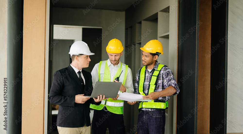 Contractor and architect looking at plan, tablet, laptop and talking about working on big project. B