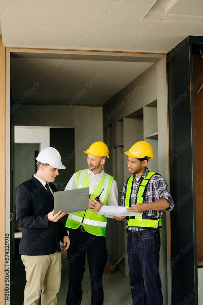 Contractor and architect looking at plan, tablet, laptop and talking about working on big project. B