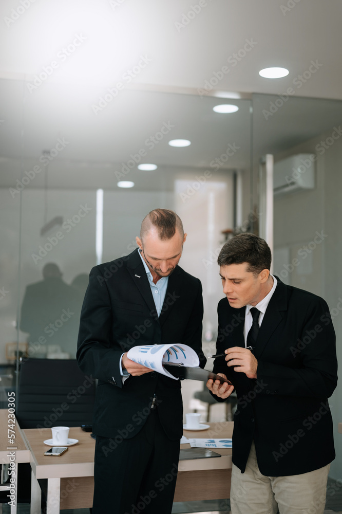 Male discussing new project with male colleague. Mature man talking with young man in office.