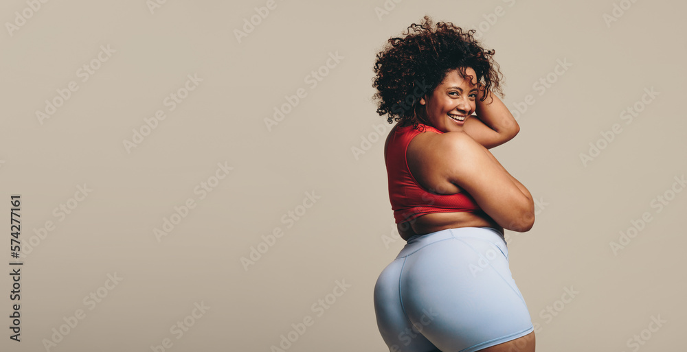 Young plus-size woman embracing athletic confidence as she stands in a studio wearing sports clothin