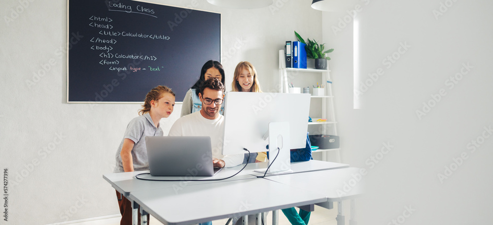 Elementary school teacher leading a coding lesson in a classroom, using a computer to show his stude