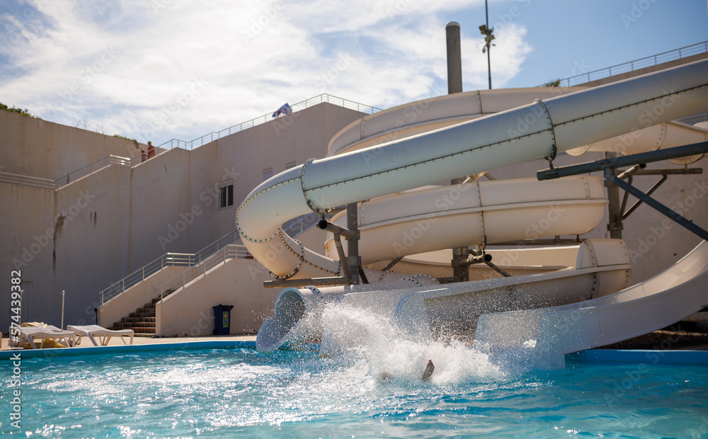 Someone unknown goes down the slide and splashes water in the pool in the water park