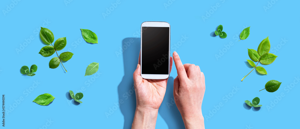 Person using a smartphone with green leaves - flat lay