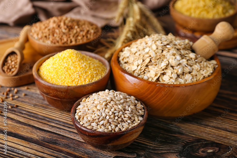 Bowls with different cereals on wooden background, closeup