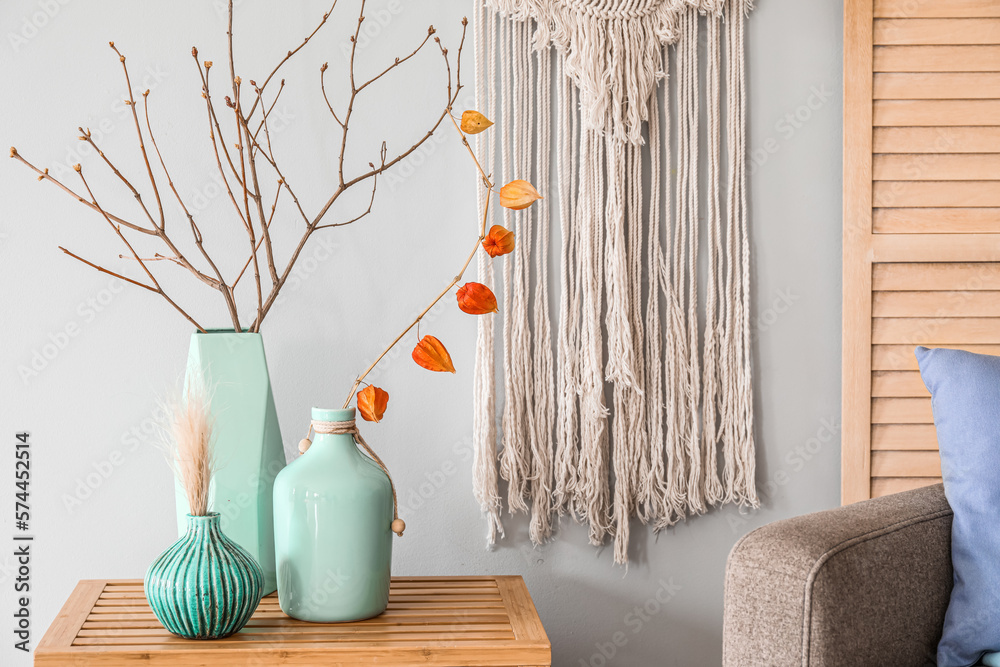 Vases with tree branches on wooden table near light wall