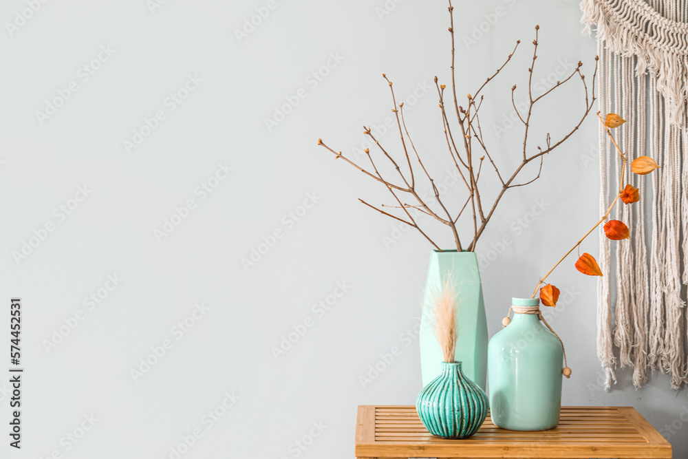 Vases with tree branches on wooden table near light wall