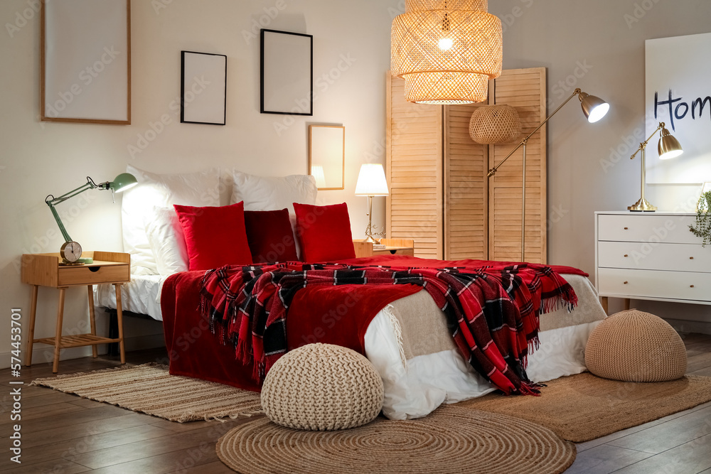 Interior of bedroom with red checkered blankets on bed and glowing lamps late in evening