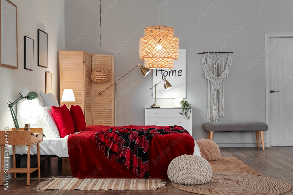 Interior of bedroom with red checkered blankets on bed and glowing lamps late in evening