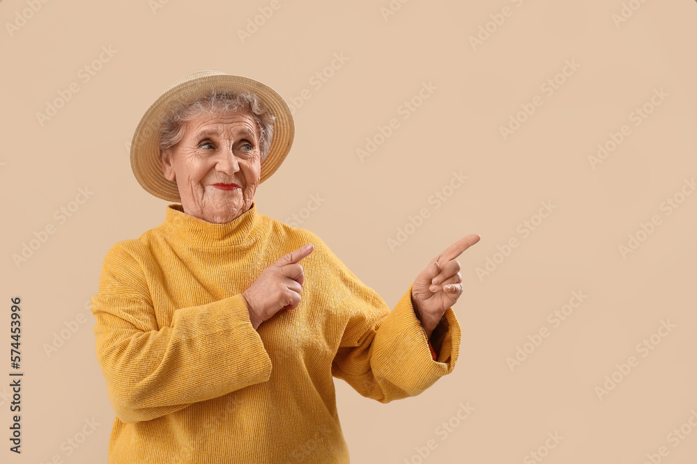 Senior woman in hat pointing at something on beige background