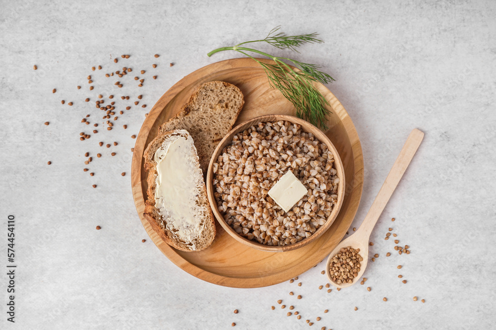 Wooden bowl of tasty buckwheat porridge with butter, bread and dill on grey table