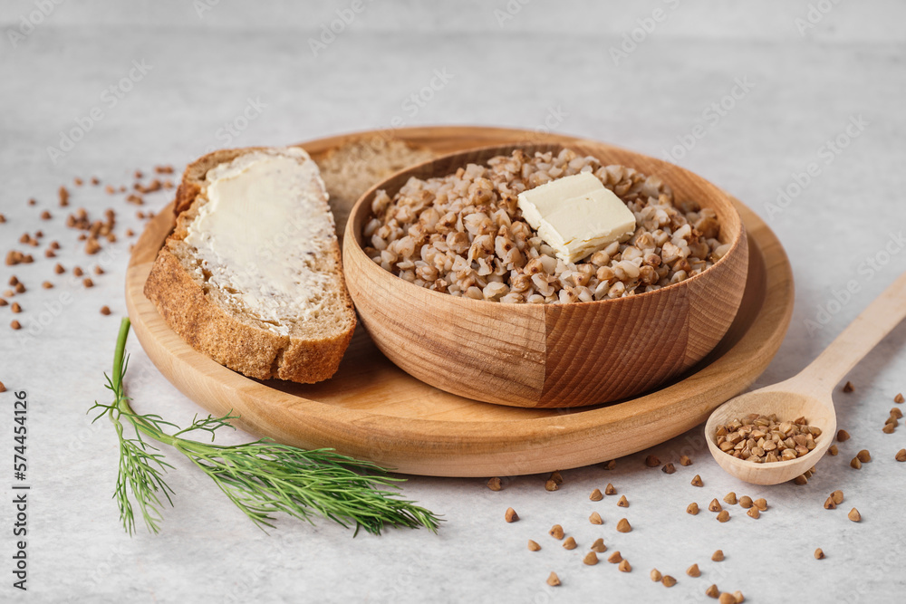 Wooden bowl of tasty buckwheat porridge with butter, bread and dill on grey table