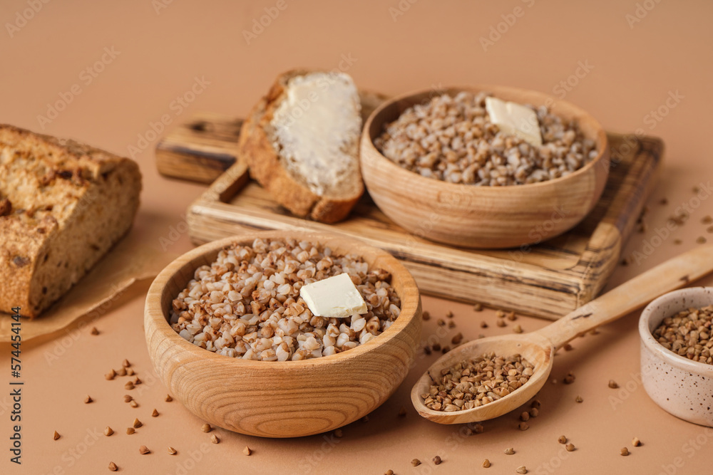 Wooden bowls of tasty buckwheat porridge with butter and bread on beige background