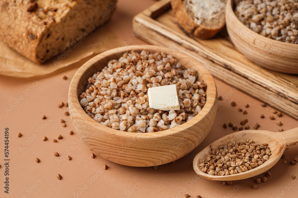 Wooden bowl of tasty buckwheat porridge with butter on beige background