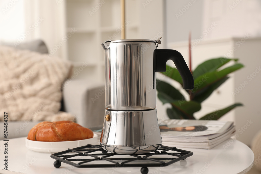 Grid with geyser coffee maker and delicious croissant on table in living room