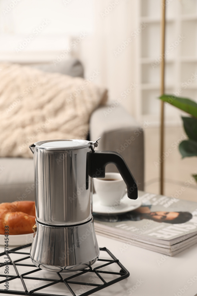 Grid with geyser coffee maker and delicious croissant on table in living room