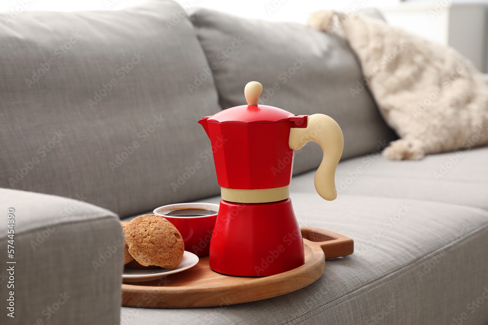 Board with geyser coffee maker, cup of espresso and cookies on sofa