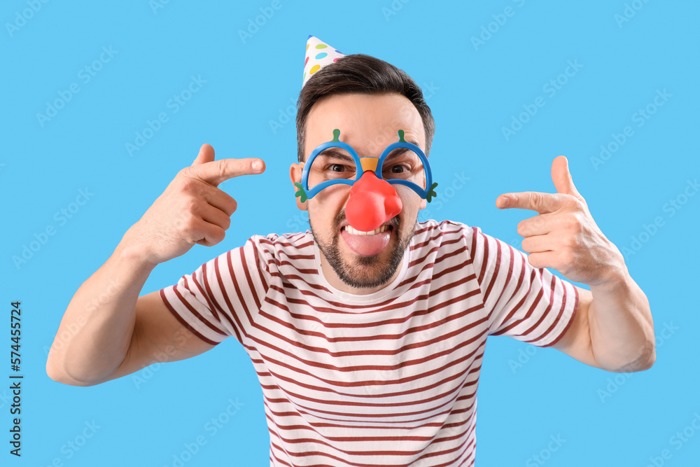 Funny young man pointing at disguise on blue background. April Fools Day celebration