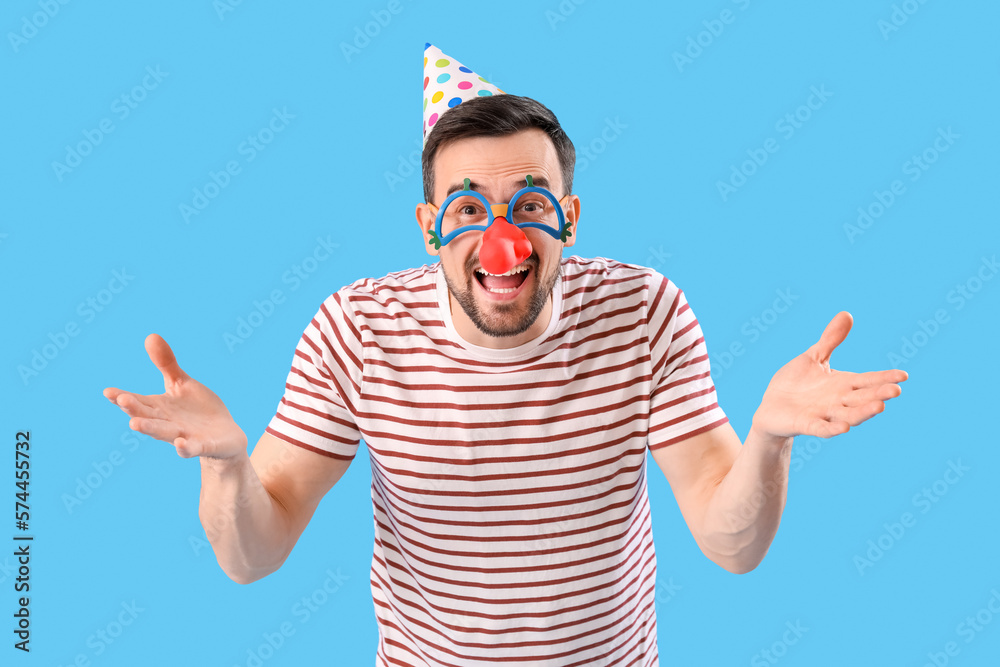 Funny young man in disguise on blue background. April Fools Day celebration