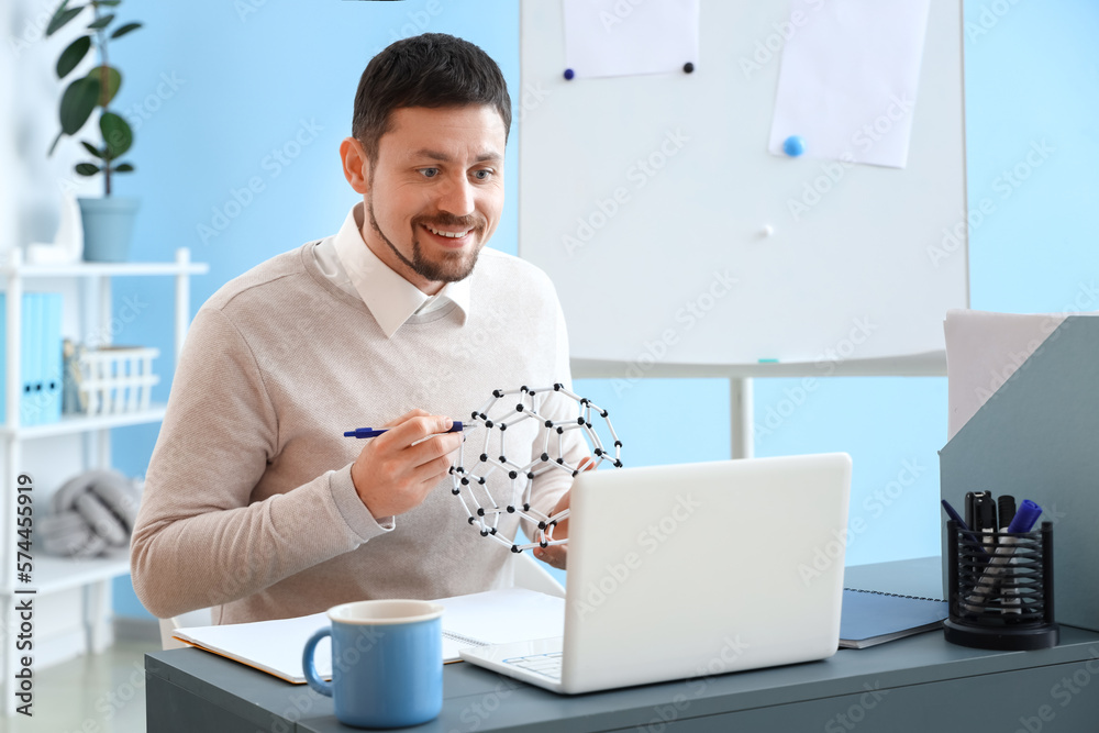 Male tutor with molecular model giving online Physics lesson at home