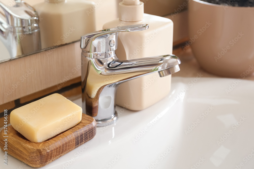 Wooden bowl with soap bar on white ceramic sink, closeup