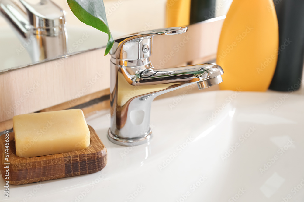 Wooden bowl with soap bar on white ceramic sink, closeup