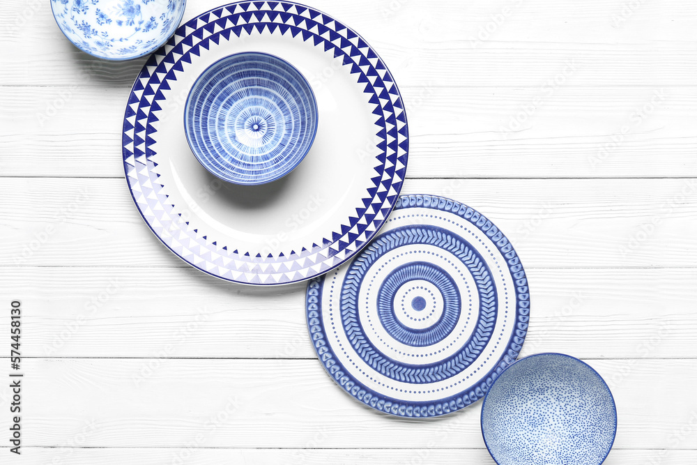 Composition with clean ceramic plates and bowls on white wooden background