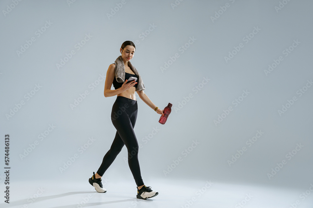 Woman use phone while walking with water bottle and towel over studio background 