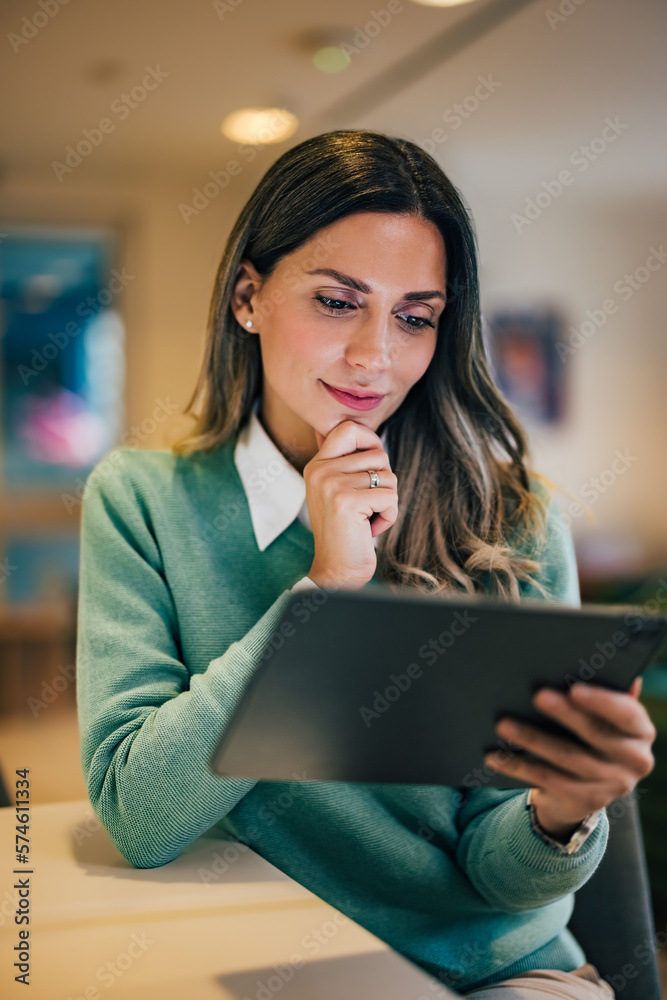 Smiling businesswoman using a digital tablet, sitting at the home office, elegantly dressed.