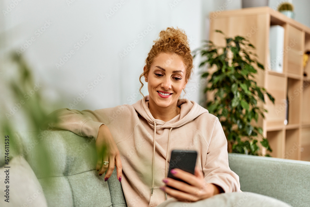 Smiling woman relaxing on the couch at home, surfing the web over the smartphone.