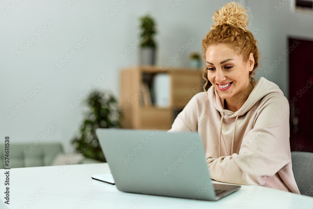 Smiling woman using a laptop, surfing the web, sitting in the living room.