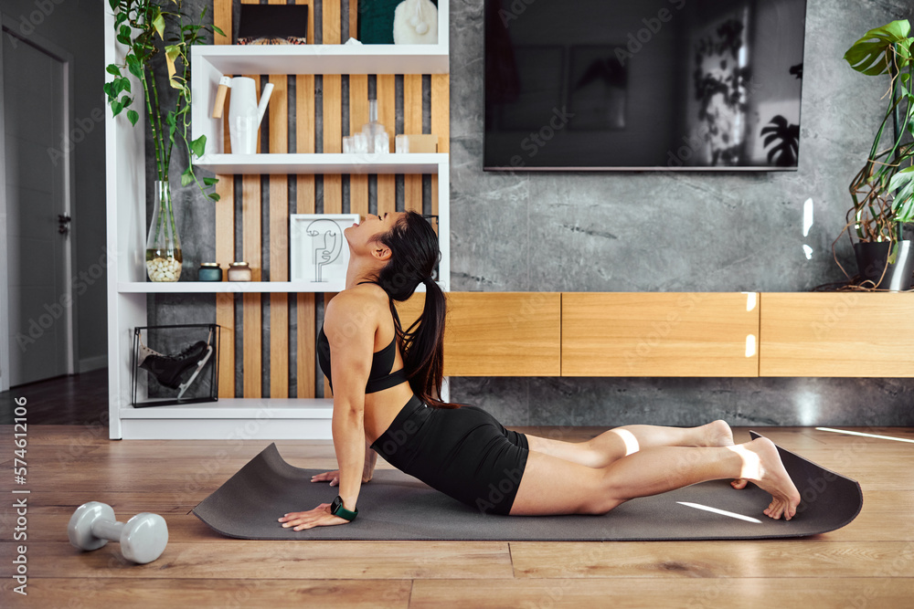 Asian woman in shape doing morning back stretching on a mat, at home.