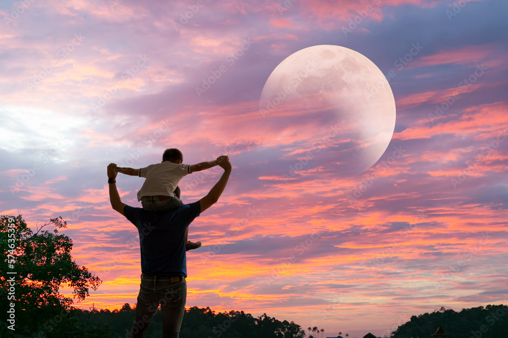 Happy Dad carrying son on shoulders looking future project with the Moon. Silhouette of father and s