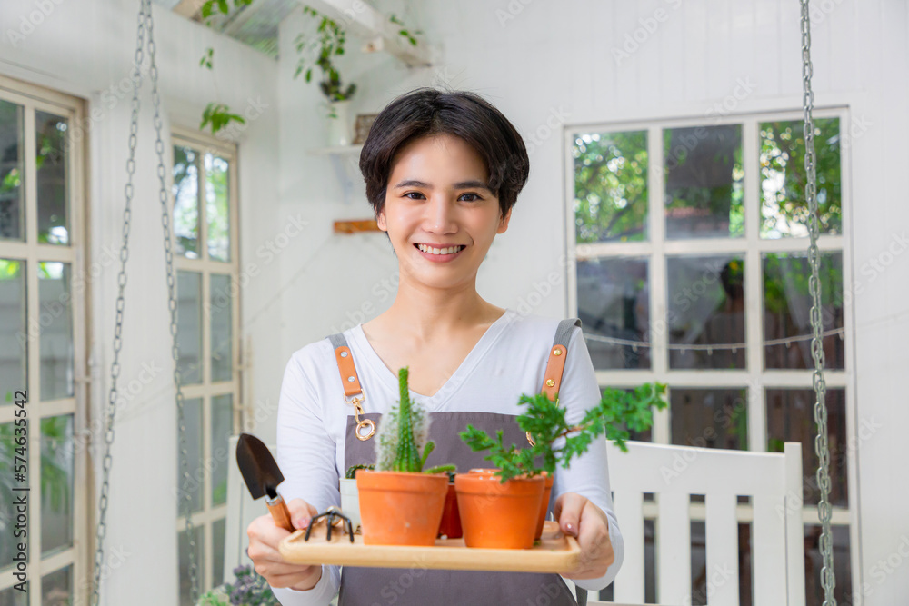 Smiling asian woman hold pot can watering green plant in office workplace. Happy female gardener or 