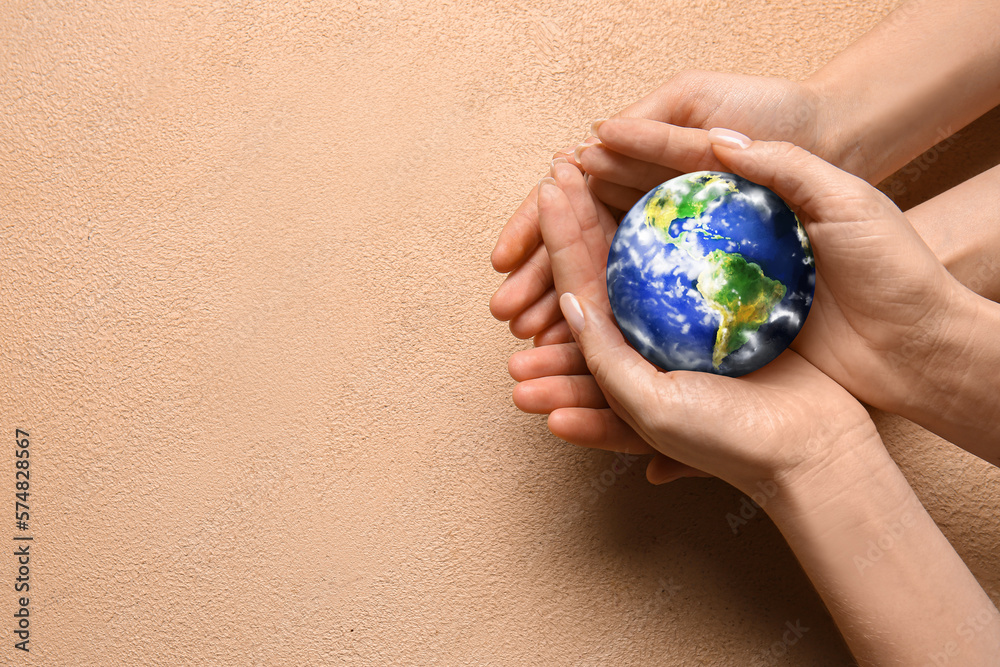 Hands of people holding small planet Earth on beige background