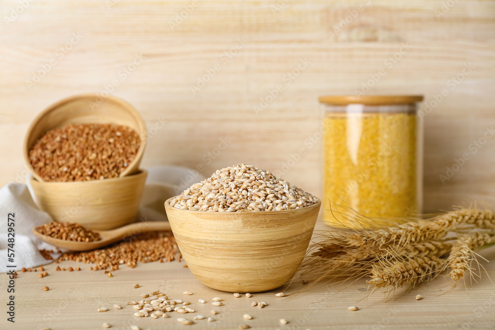 Bowl with pearl barley and spikelets on wooden background