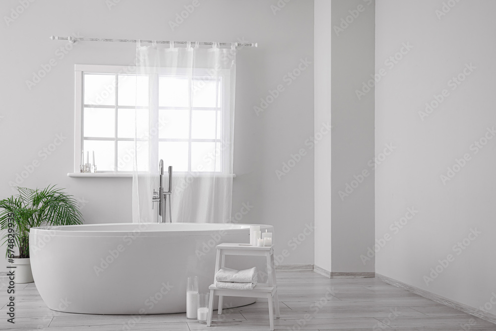 Modern bathtub, houseplant and table with candles in bathroom interior