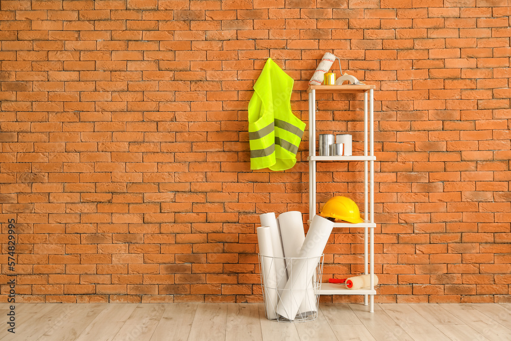 Safety vest, shelving unit with renovation supplies and hardhat near brick wall