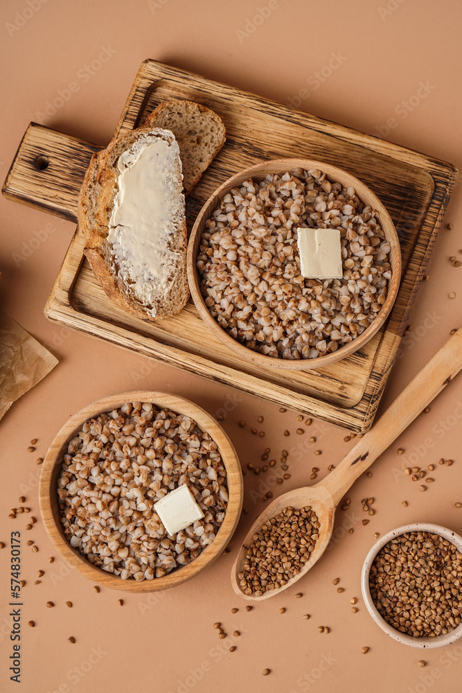 Wooden bowls of tasty buckwheat porridge with butter and bread on beige background