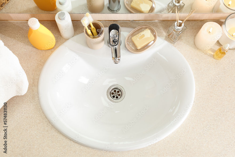 Table with white ceramic sink, burning candles and bath supplies