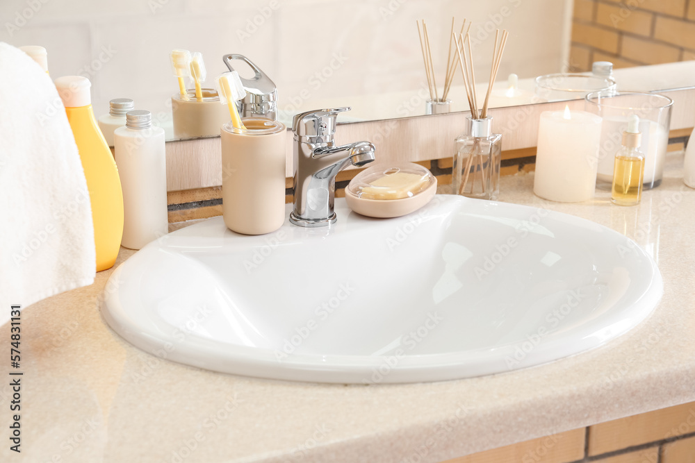 Table with white ceramic sink, burning candles and bath supplies