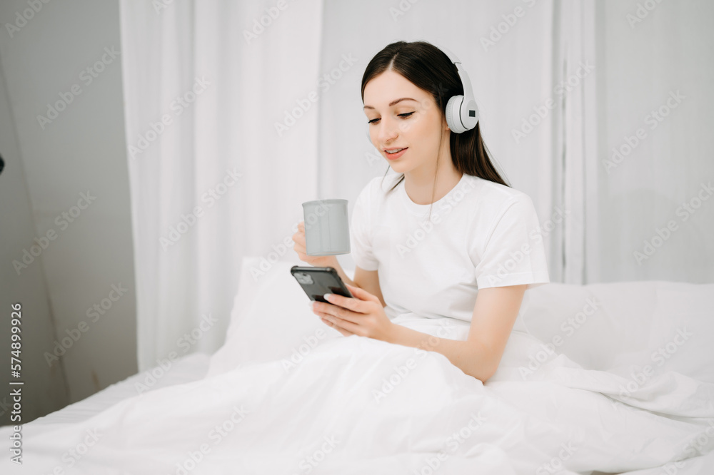 Beautiful young woman on a white bed with coffee cub and using smart phone at home. lifestyle concep