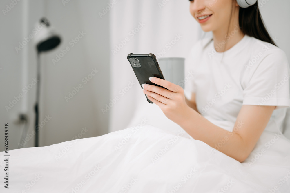 Beautiful young woman on a white bed with coffee cub and using smart phone at home. lifestyle concep