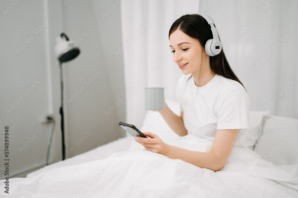 Beautiful young woman on a white bed with coffee cub and using smart phone at home. lifestyle concep