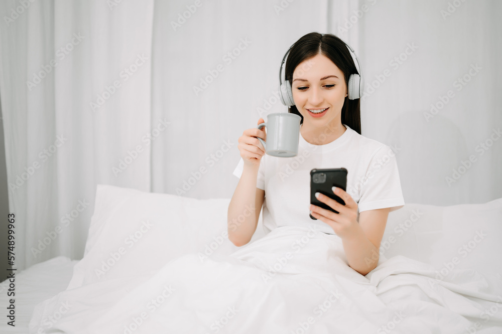 Beautiful young woman on a white bed with coffee cub and using smart phone at home. lifestyle concep