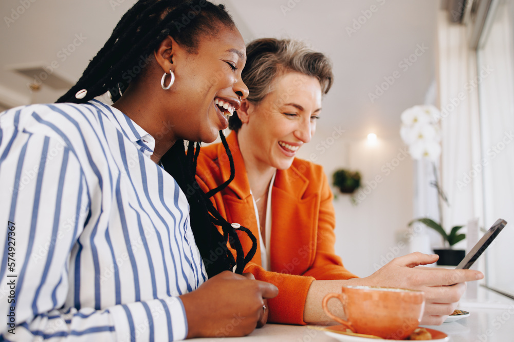 Two cheerful business women using a smartphone together in a coffee shop