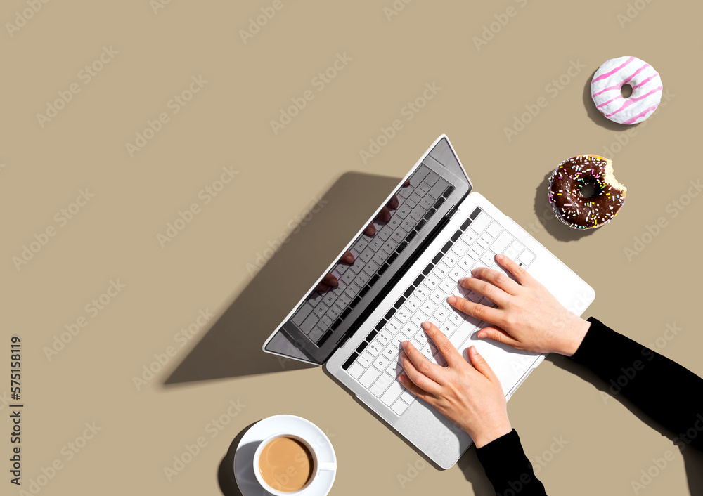 Person using a laptop computer with a donut and a cup of coffee - Flat lay