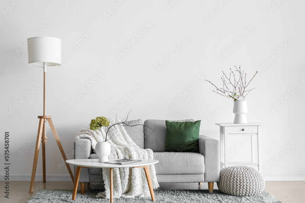 Interior of living room with sofa, flowers and tree branches in vases